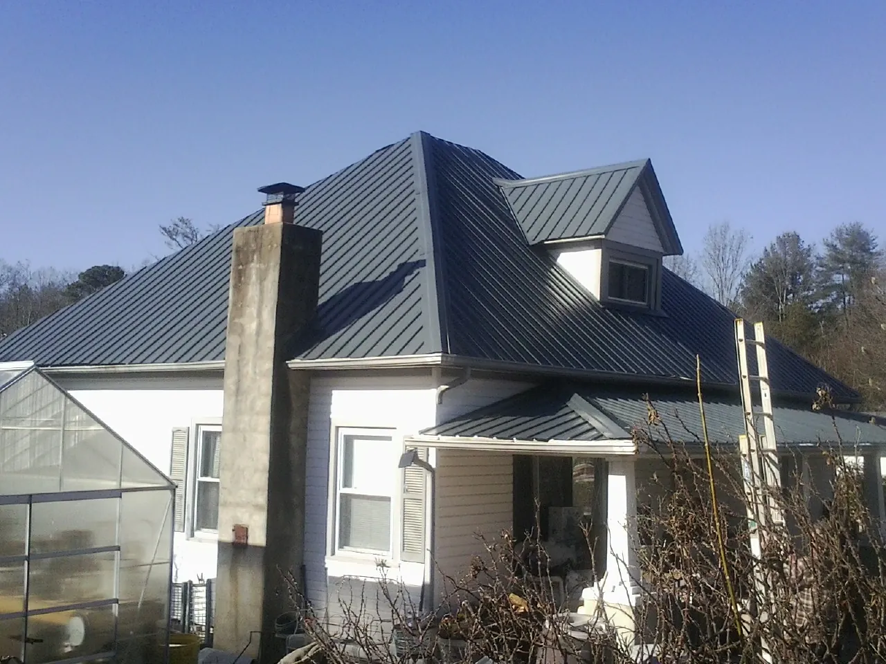Dark blue standing seam metal roof on a white farmhouse with dormer — Slate & Tile Roof Repair by Roofing Brothers in Maquoketa