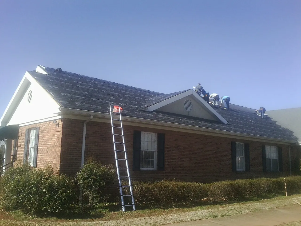 Crew tearing shingles off a brick ranch roof with a ladder set — Emergency Roof Repair work by our crew in Maquoketa