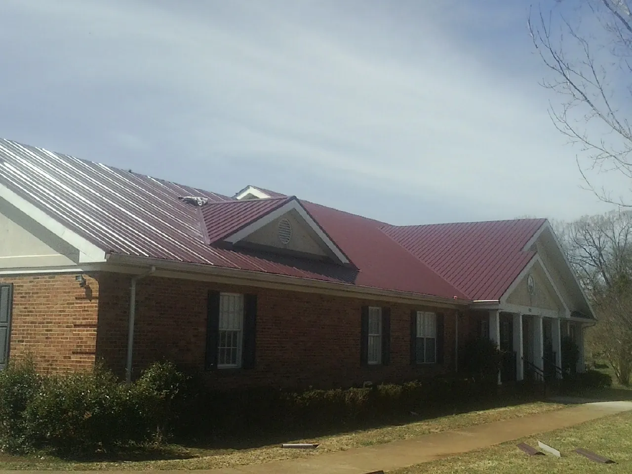 Red metal roof with gabled entries on a long brick building, from a Hail Damage Roof Repair job in Maquoketa