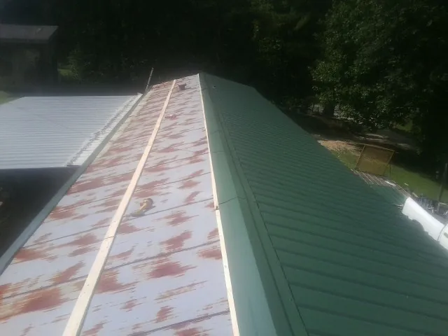 Old rusted panels beside newly installed green metal roofing — Wind Damage Roof Repair by Roofing Brothers in Maquoketa