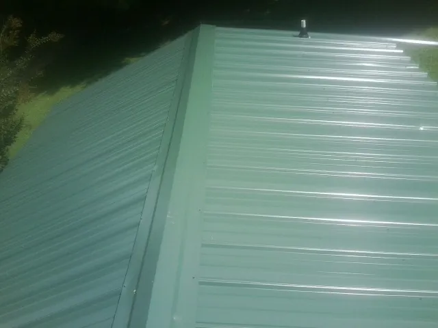 New green metal panels meeting at the ridge of a roof — Flat Roof Repair work by our crew in Maquoketa