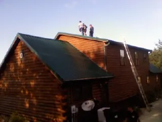 Crew on the ridge of a green metal roof on a two story log home in Maquoketa
