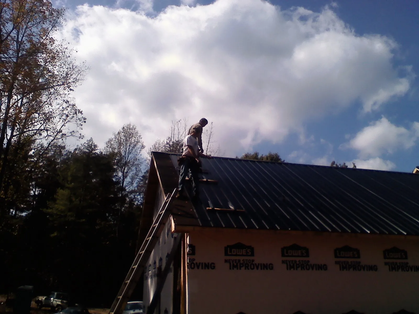Roofer fastening dark metal panels high against a cloudy sky, from a Roof Inspection job in Maquoketa