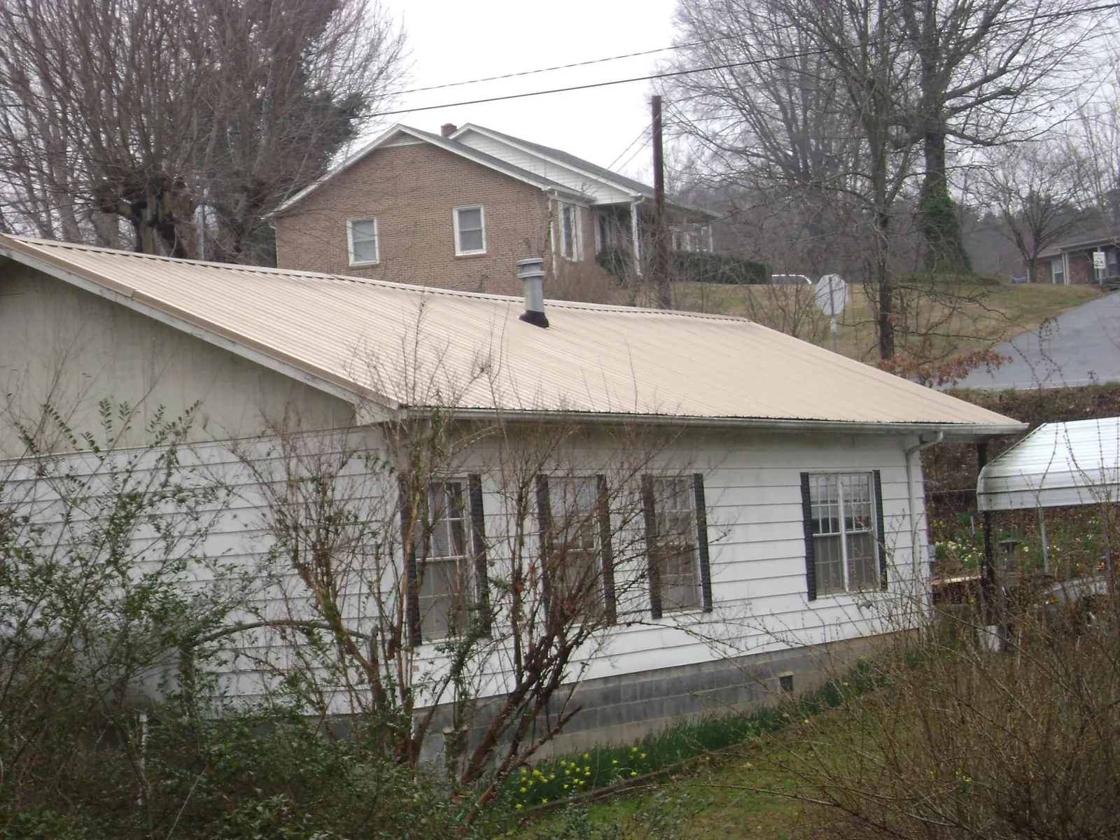 Tan metal roof on a white sided house set into a hillside — Commercial Roofing by Roofing Brothers in Maquoketa