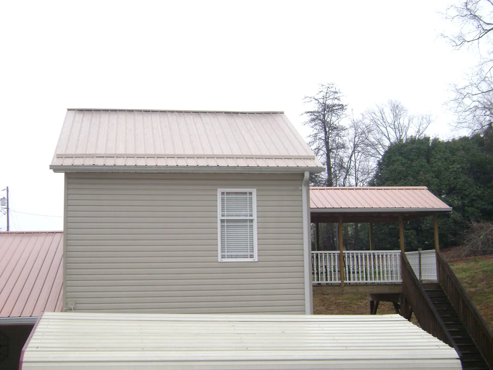 Tan metal roofs on a two story addition and attached porch, from a Roof Replacement job in Maquoketa